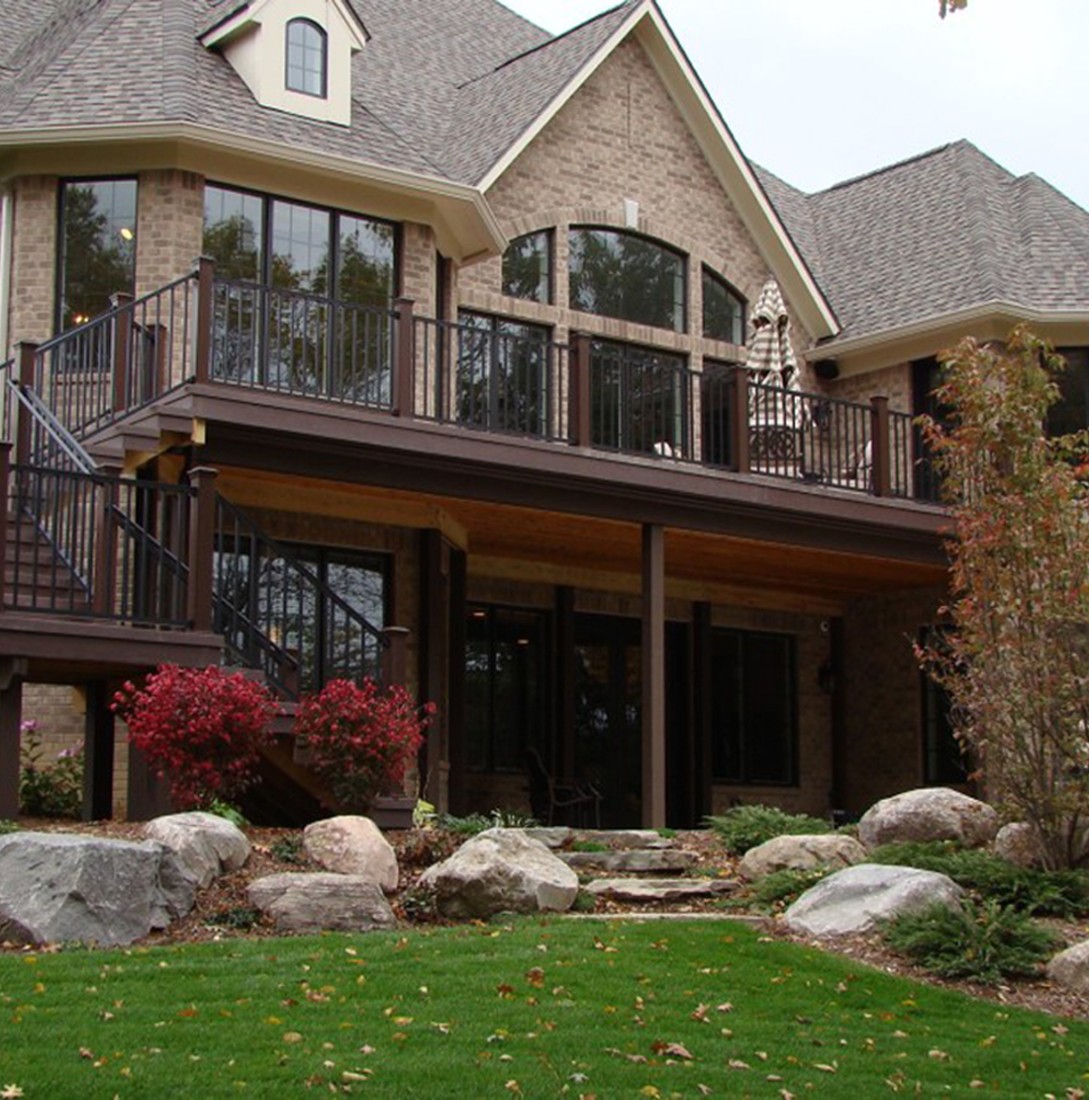 Modern brick house with a large deck and black metal railing.